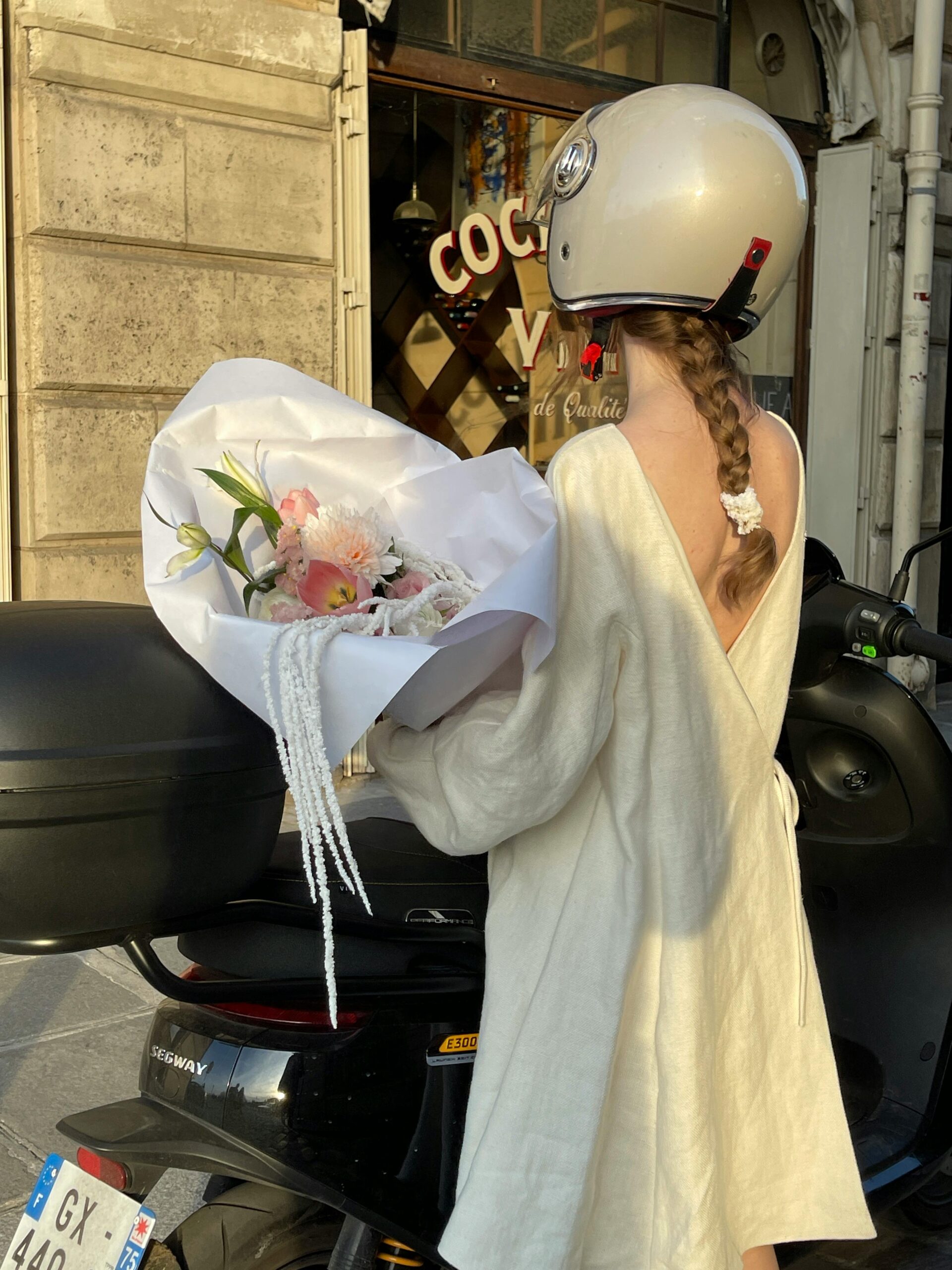 Woman in cream dress holding a bouquet while seated on a scooter, wearing a helmet—symbolizing creative entrepreneurs navigating modern marketing beyond social media.