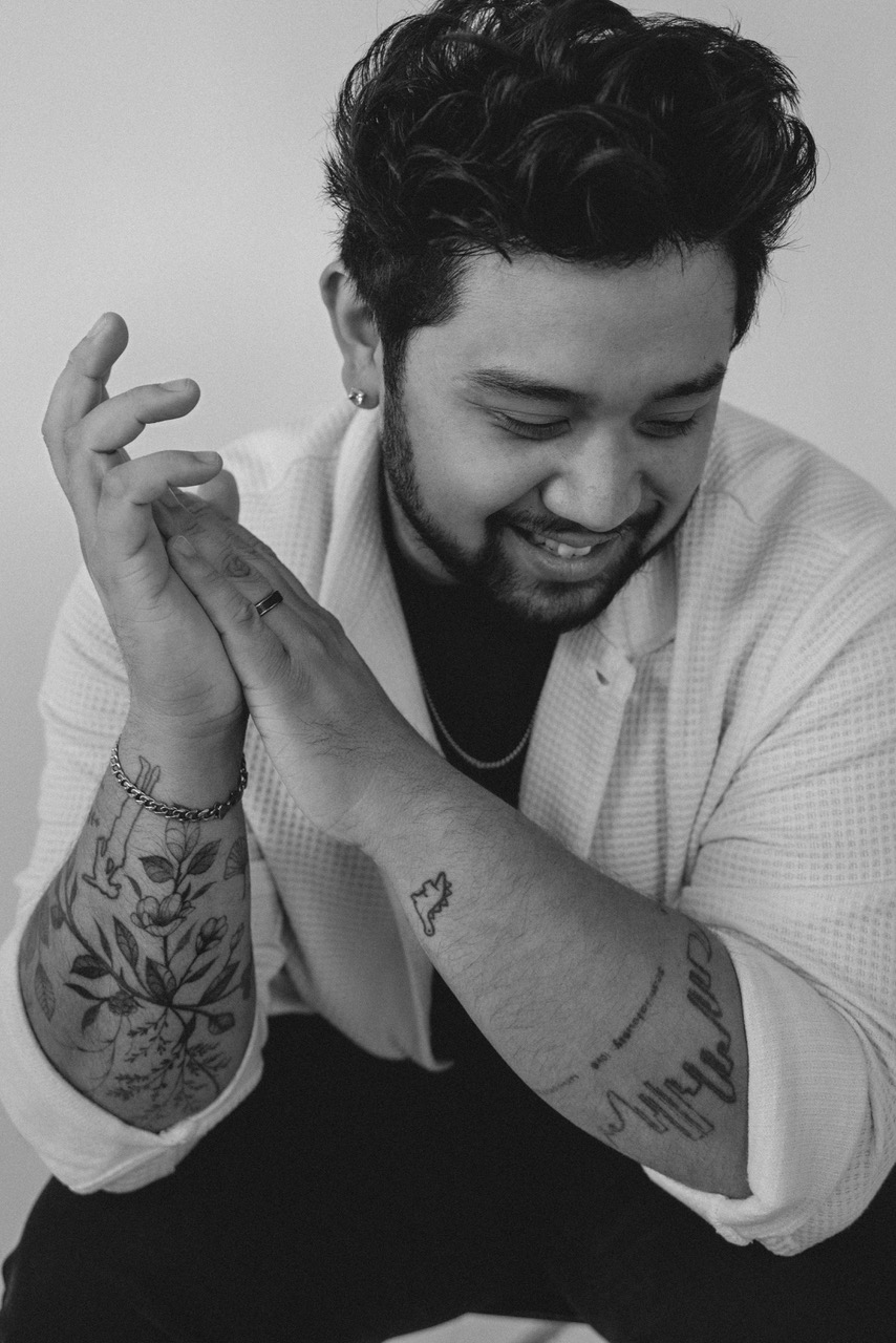 Black and white portrait of Ean Cuenca of Cuenca Creative smiling with his hands together, showing detailed tattoos on his arms