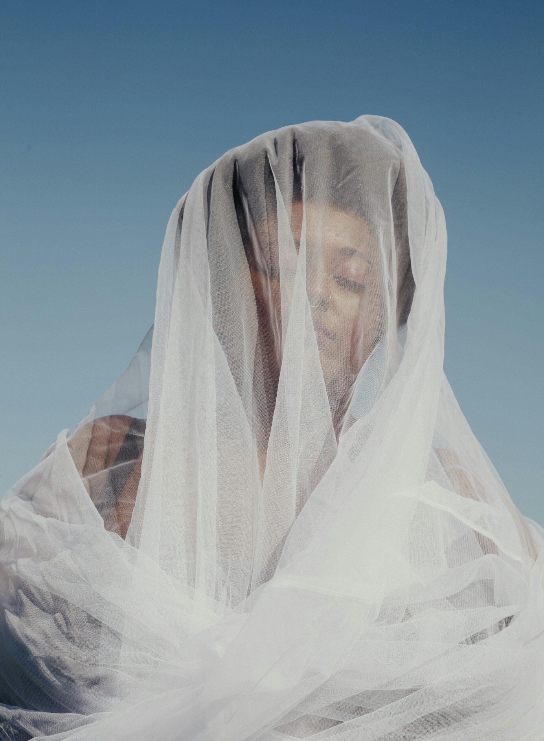 Close-up of a person wrapped in flowing white fabric against a blue sky, representing clarity, mystery, and the unseen layers of AI visibility in modern branding.